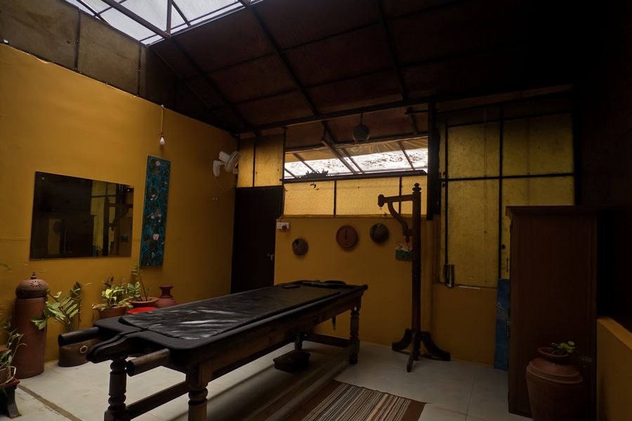 Inside the Ayurveda spa, a wooden treatment table beneath a skylight, with a mirror and brass vessels along the wall.