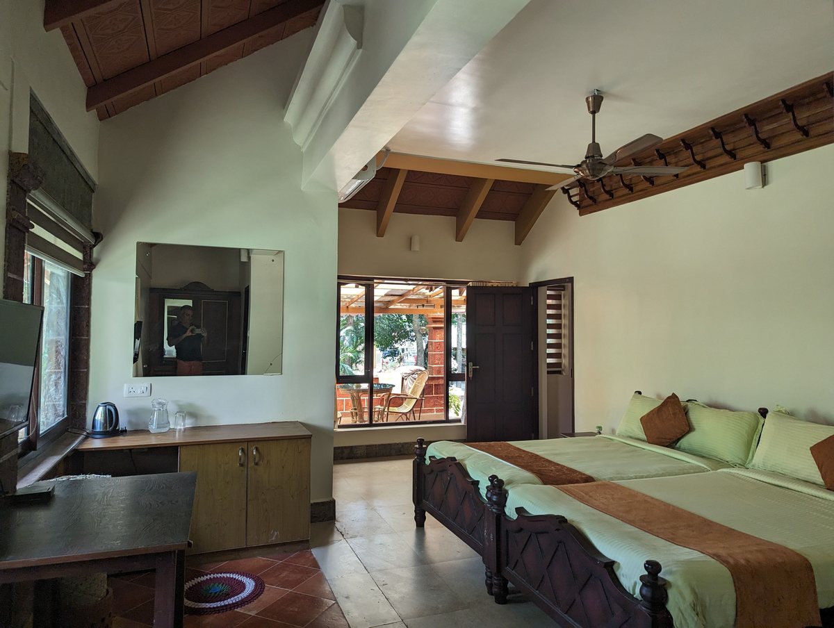 A family suite bedroom with twin beds pushed together, a high beamed ceiling and a wide window onto the garden.