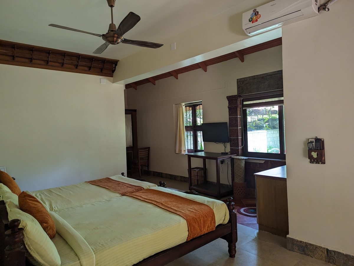 A superior room with a wide bed, a ceiling fan and air conditioning, and a window onto the trees.