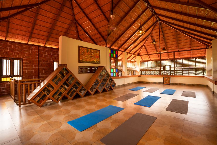 A yoga hall under a peaked tiled roof, mats laid out on the floor beside built-in bookshelves and a mural.